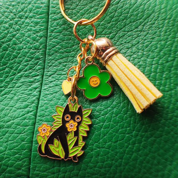 Porte-clé chat noir avec hautes herbes et fleurs jaunes, pompon jaune clair sur sac en cuir vert