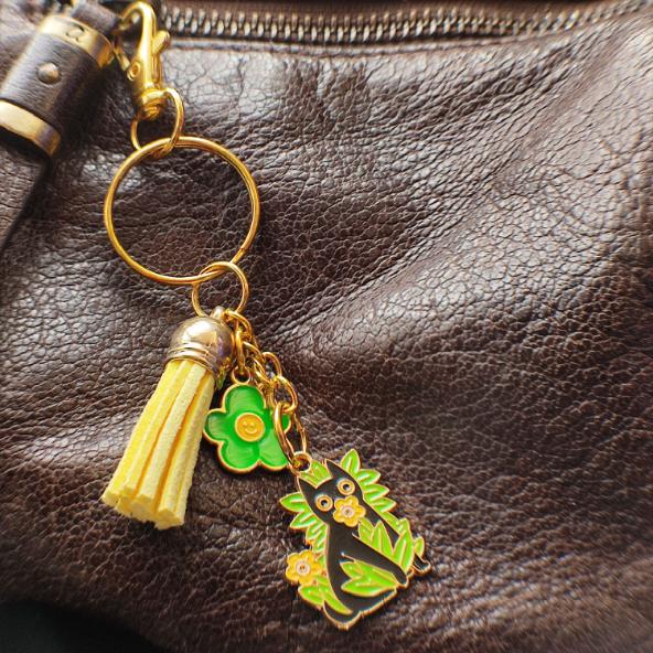 Porte-clé chat noir avec hautes herbes et fleurs jaunes, pompon jaune clair sur sac en cuir marron
