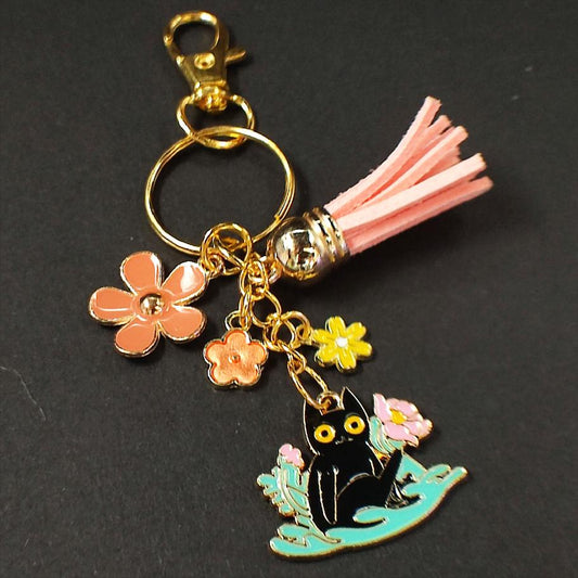 Porte-clé Chat Noir dans un parterre de fleurs roses avec pompon rose.