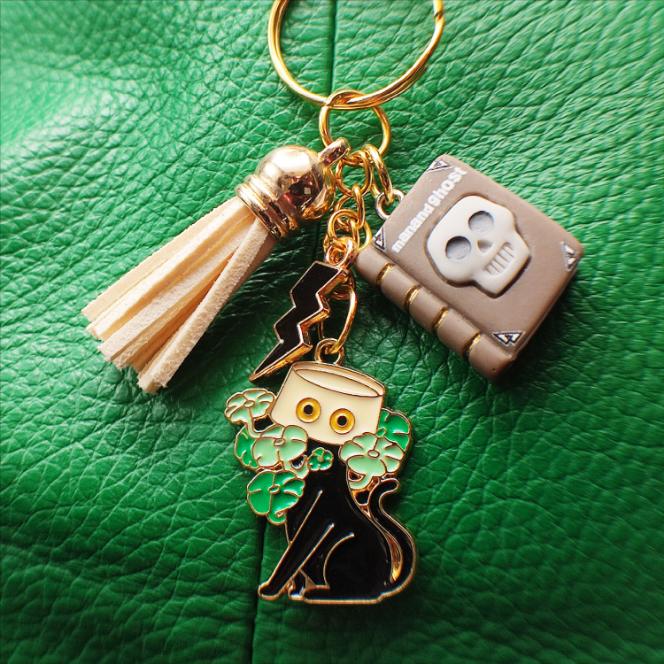 Porte-clé chat noir avec livre "Man and Ghost", pot jaune, pompon beige sur sac vert