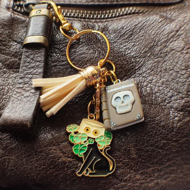 Porte-clé chat noir avec livre "Man and Ghost", pot jaune, pompon beige sur sac marron