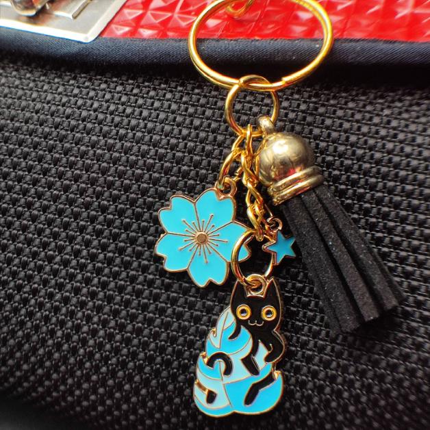 Porte-clé chat noir caché derrière une feuille bleue avec pompon bleu ou noir