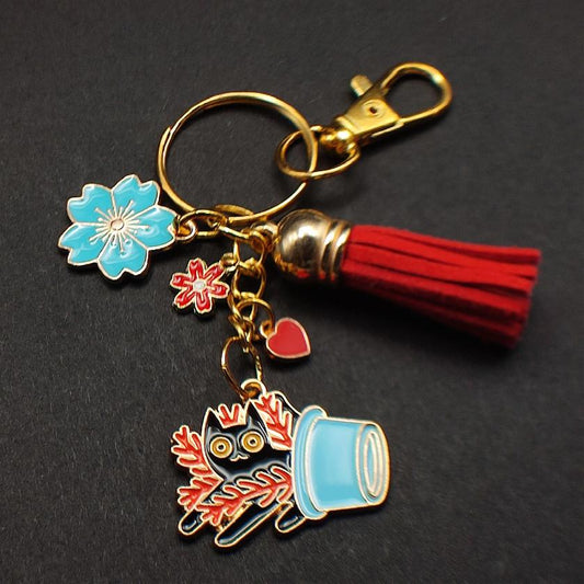 Porte-clé chat noir dans pot bleu renversé avec plante rouge, pompon rouge