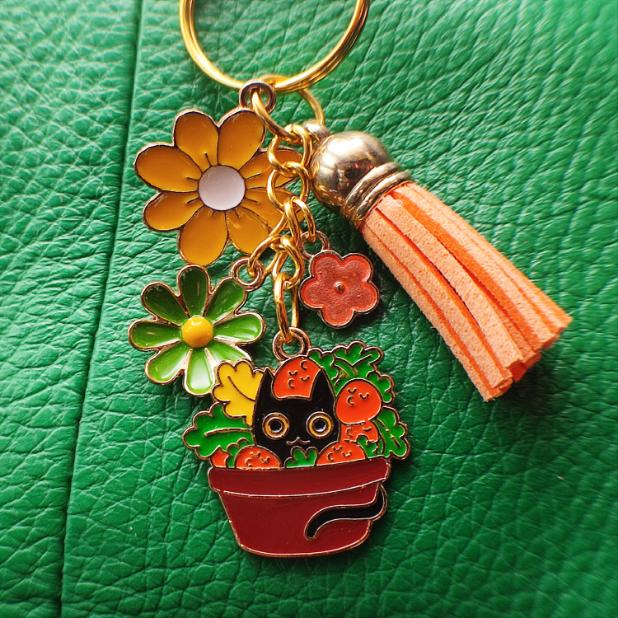 Porte-clé chat noir dans un pot de champignons colorés, pompon orange sur sac cuir vert