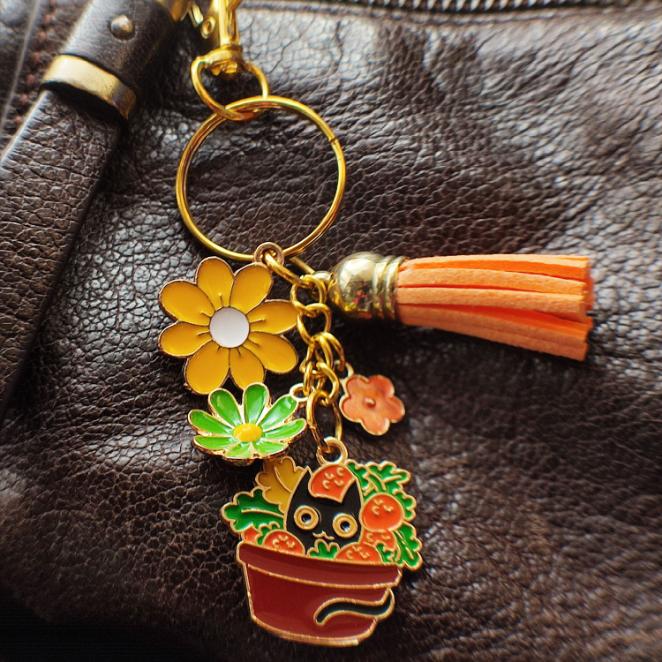 Porte-clé chat noir dans un pot de champignons colorés, pompon orange sur sac cuir marron