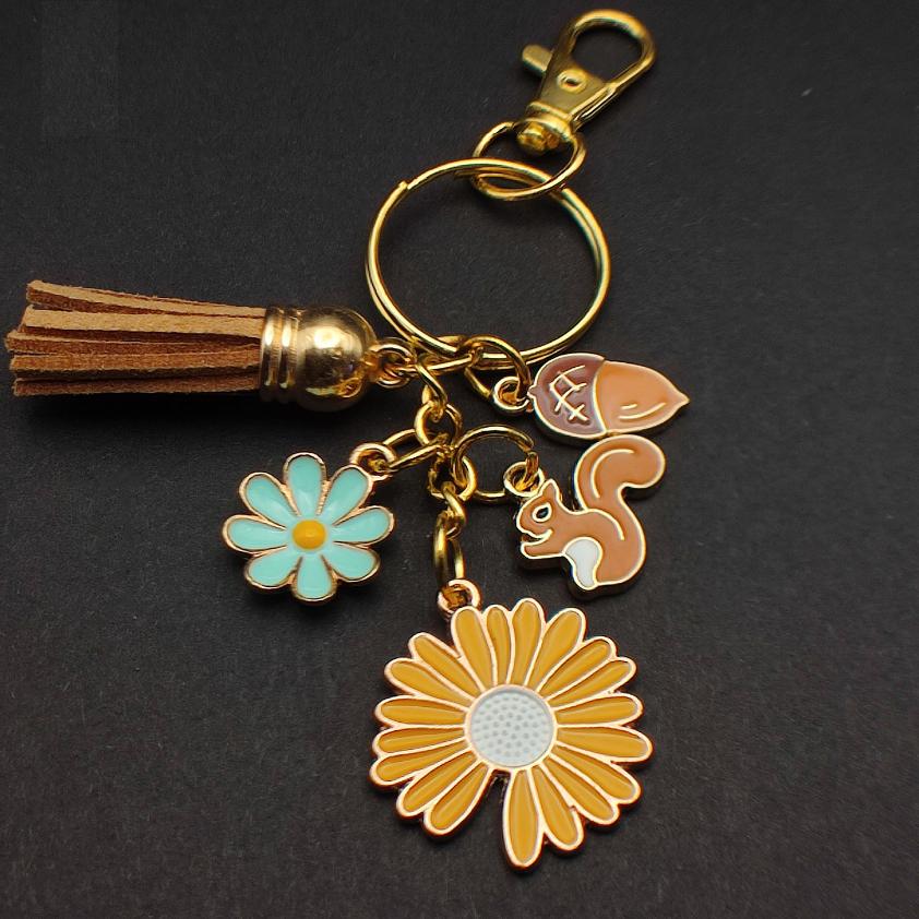Porte-clé avec écureuil marron clair, gland et fleurs jaunes et bleues.
