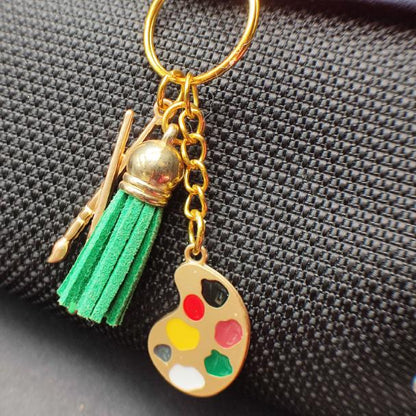 Porte clé Original en métal émaillé avec pompon en cuir, représentant une palette de peintre et des pinceaux, vue esthétique sur un sac noir