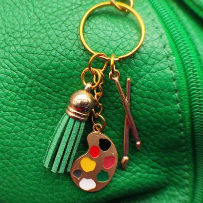 Porte clé Original en métal émaillé avec pompon en cuir, représentant une palette de peintre et des pinceaux, vue esthétique sur un sac en cuir vert