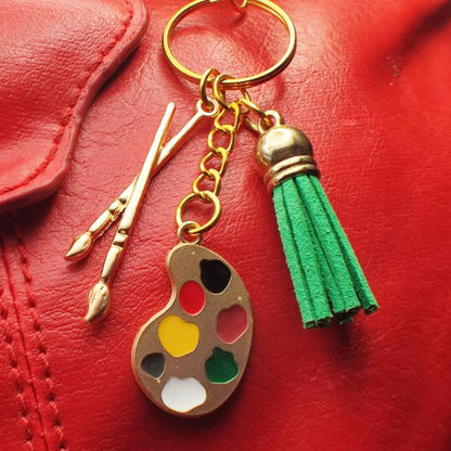 Porte clé Original en métal émaillé avec pompon en cuir, représentant une palette de peintre et des pinceaux, vue esthétique sur un sac en cuir rouge