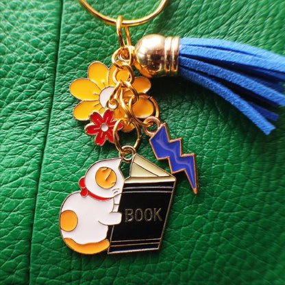 Détail 1 porte clé Chat blanc et jaune kawaii avec un livre noir et des fleurs 