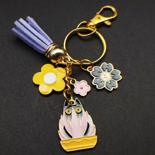    Porte-clé chat noir dans un pot jaune avec plante rose et mauve, pompon mauve.

