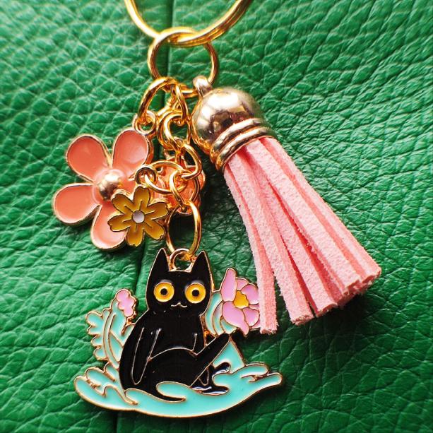 Porte-clé Chat Noir dans un parterre de fleurs roses avec pompon rose sur sac vert