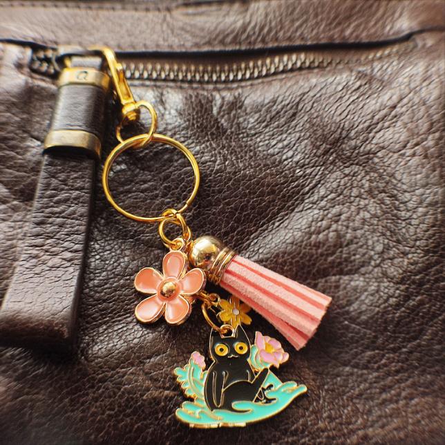 Porte-clé Chat Noir dans un parterre de fleurs roses avec pompon rose sur sac marron