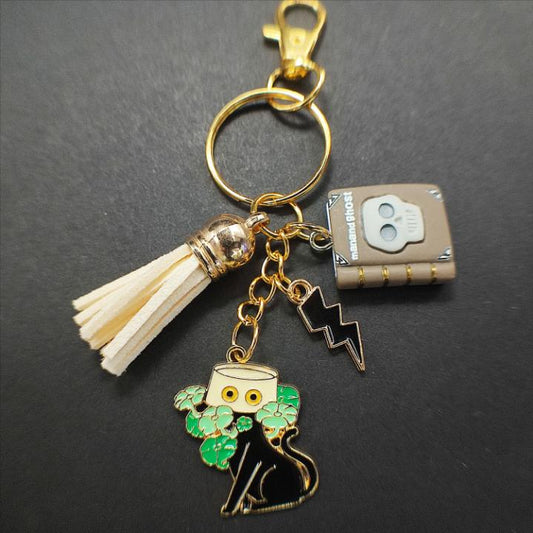Porte-clé chat noir avec livre "Man and Ghost", pot jaune, pompon beige
